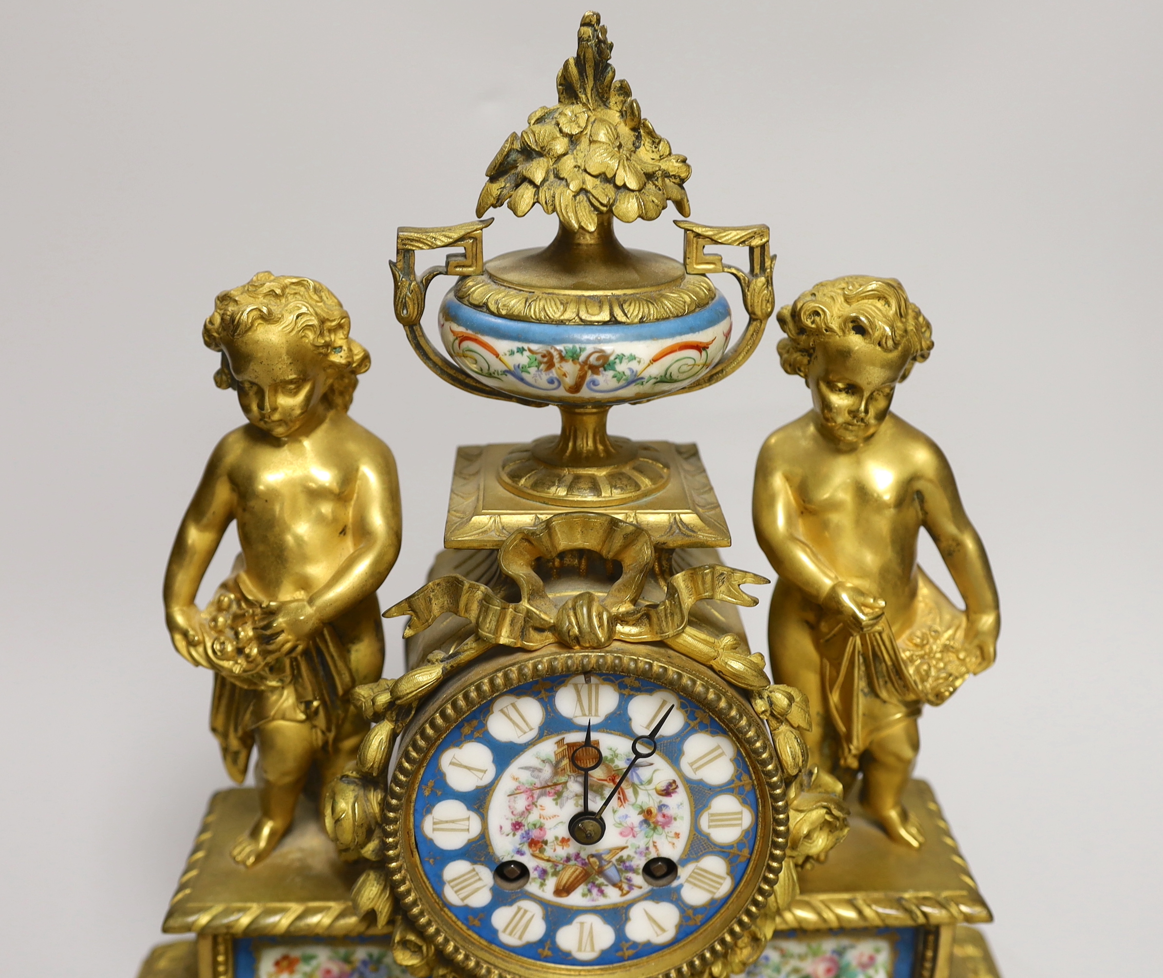 A French decorative ormolu putti mantel clock with porcelain clock face, side panels and urn